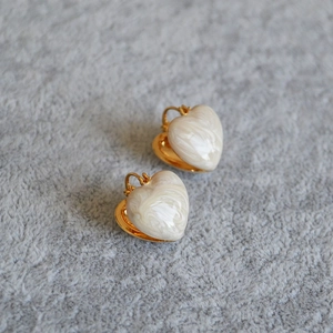 Detailed macro view of heart-shaped gold-plated earrings with white enamel marble texture