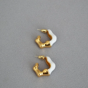 Macro detail of wave-shaped C-hoop earrings featuring gold plating and white enamel finish