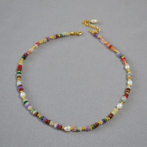 Dettaglio di perle in pietra colorata e perle barocche su una collana con chiusura oro