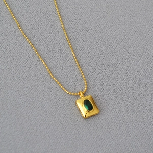 Gros plan sur une chaîne à billes dorée avec un pendentif en pierre verte émeraude