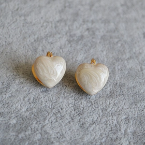 Detail of gold-plated brass heart earrings with white marble enamel on soft fur background