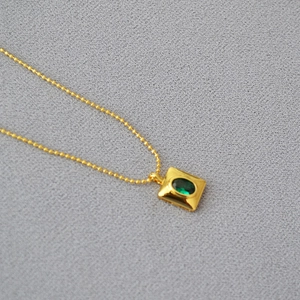 Détail macro du pendentif carré en laiton doré avec une pierre précieuse verte ovale