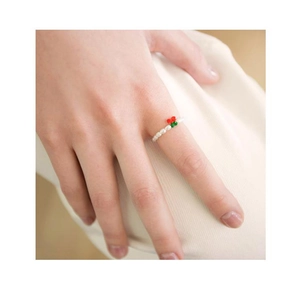Close-up of beaded pearl ring with red cherry charm on finger against soft fabric