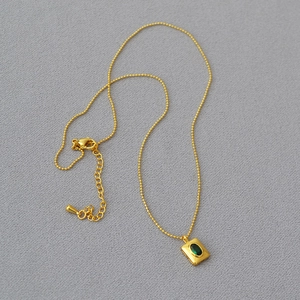 Gros plan sur collier perlé doré avec pendentif émeraude verte sur fond de tissu
