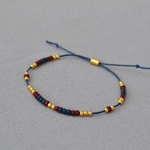 Minimalist beaded bracelet with red, blue, and gold beads on a dark blue woven cord