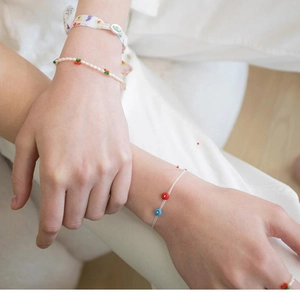 Close-up of a minimalist pearl bracelet with cherry charm and a slim colorful beaded cord
