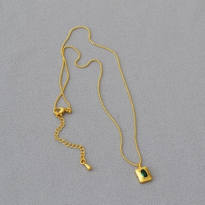 Collier élégant en laiton doré avec pendentif émeraude sur tissu gris texturé