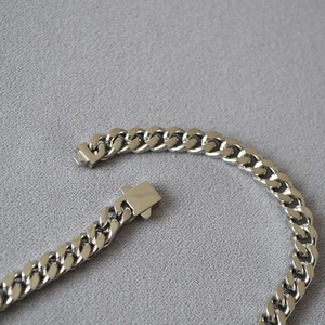 Detailed macro view of the sturdy clasp on this silver-toned stainless steel Cuban link chain