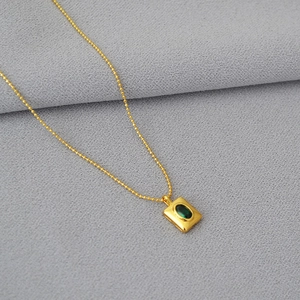 Gros plan d'un pendentif émeraude sur une chaîne à billes dorée sur tissu gris