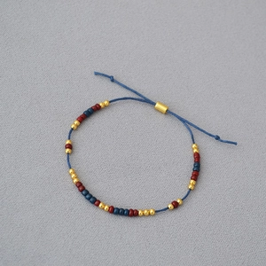 Detail of adjustable blue woven bracelet with red and gold beads on a soft grey fabric