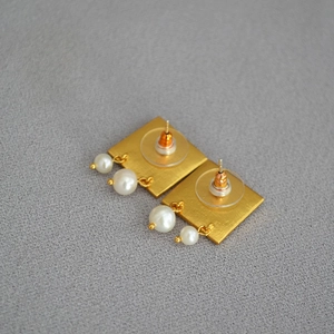Détail de boucles d'oreilles carrées dorées avec perles blanches et fermoirs en plastique