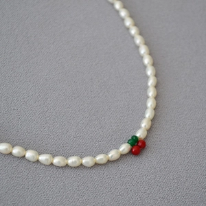 Détail d'un collier en perles d'eau douce avec pendentif cerise sur tissu texturé