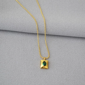 Détail macro d'un pendentif émeraude vintage sur une fine chaîne à billes dorée