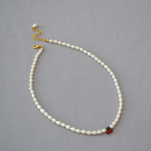 Détail d'un collier en perles d'eau douce avec un pendentif cerise rouge perlé
