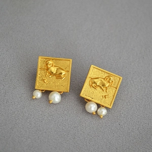 Détail de boucles d'oreilles carrées dorées avec relief de chien et perles d'eau douce