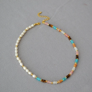 Detail of beaded necklace with white pearls and multicolored stones on grey background