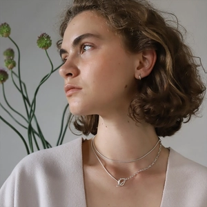 Close-up of a double-layered silver necklace featuring a snake chain and T-bar toggle clasp