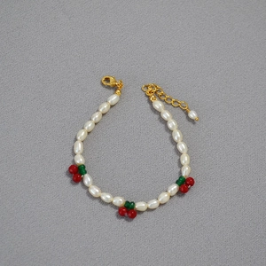 Detail of red cherry charms on freshwater pearl bracelet with golden lobster clasp