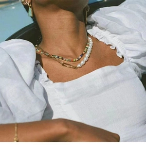 Detail of colorful beads, vintage pearls and gold paperclip chain necklace on model