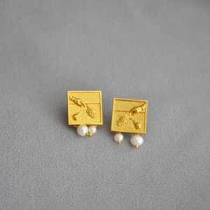 Détail de boucles d'oreilles carrées dorées avec motif en relief et perles naturelles