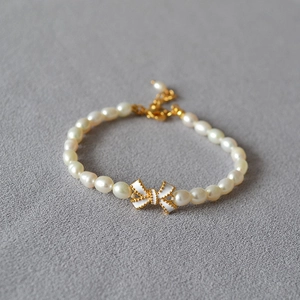 Nahaufnahme von Süßwasserperlenarmband mit weißer Emaille-Schleife und Goldverschluss