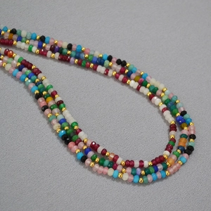 Detail of bohemian colorful faceted bead necklace with gold spacer beads on gray cloth