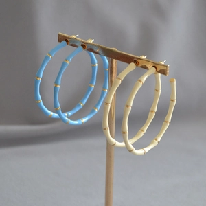 Detail of bamboo joint style hoop earrings in sky blue and beige enamel on a stand