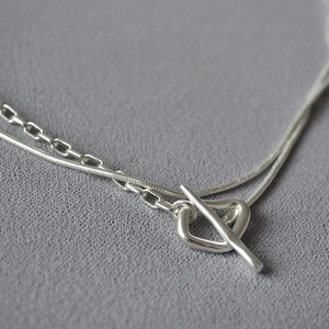 Macro shot of silver double-layered necklace featuring snake chain and T-bar heart toggle