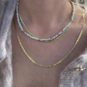 Detail of layered blue stone beaded necklace and flat gold snake chain on a model