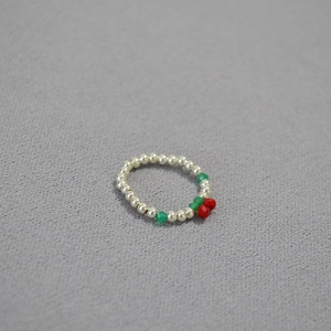 Detailed close-up of a beaded cherry ring with silver, red, and green beads on gray fabric