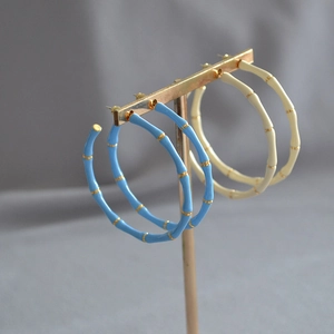 Detailed close-up of bamboo-style hoop earrings in blue and cream with gold trim accents