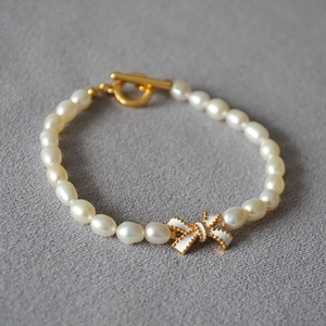 Detailansicht eines Perlenarmbands mit weißer Emaille-Schleife und goldenem OT-Verschluss