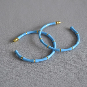 Chic light blue enamel bamboo hoop earrings with gold metal accents on textured fabric