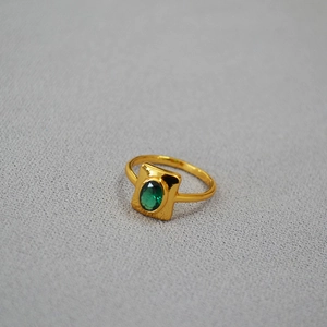 Détail d'une bague rétro en laiton doré avec émeraude verte sur tissu texturé