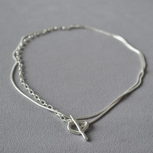 Close-up of double-layered silver necklace featuring sleek snake and link chains with OT clasp