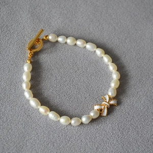 Elegantes Armband mit weißen Emaille-Schleifen und Süßwasserperlen sowie Goldverschluss