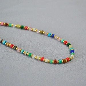 Close-up of colorful stone cylinder beads with gold spacer beads on a textured grey fabric