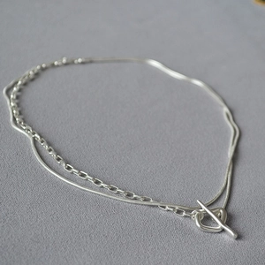 Close-up of double-layered silver snake and cross chain with T-bar toggle clasp detail
