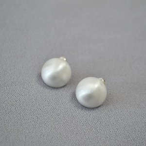 Detailed macro shot of round matte brushed pearl earrings with gold metal studs