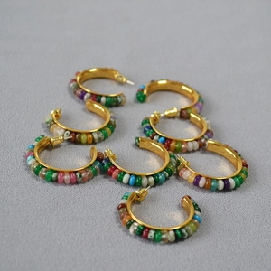 Colorful gemstone beaded C-shaped hoop earrings with gold finish on grey textured background