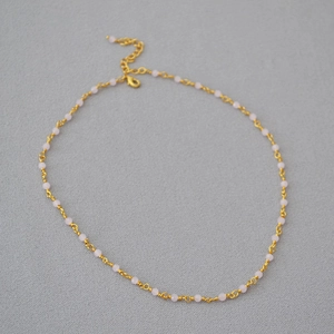 Detailed shot of the gold link chain featuring soft pink beads and lobster clasp