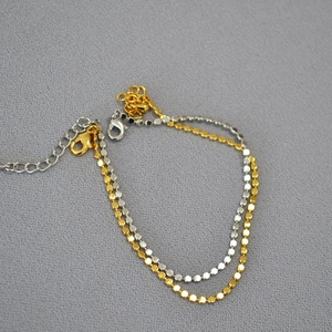Macro detail of minimalist gold and silver disc chain bracelet with lobster clasp