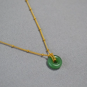 Collier perlé plaqué or avec un pendentif donut en jade vert sur fond gris texturé