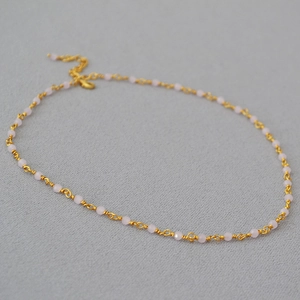 Close-up of thin gold woven necklace with pink faceted beads and lobster clasp closure