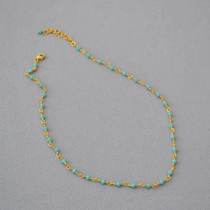 Macro shot of gold-plated chain necklace with turquoise beads and lobster clasp detail