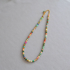 Detail of colorful beaded necklace with gold spacers and lobster clasp on grey fabric