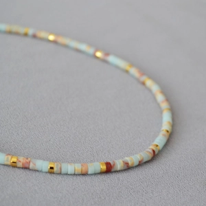 Detail of oceanic blue stone beads and gold metal discs in a minimalist beaded necklace