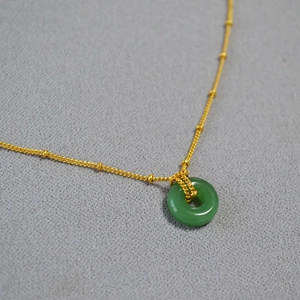 Gros plan détaillé d'un pendentif en jade vert sur une fine chaîne perlée dorée