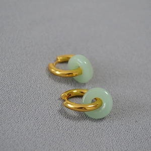 Détail macro de créoles dorées avec pendentifs donuts en jade vert clair poli