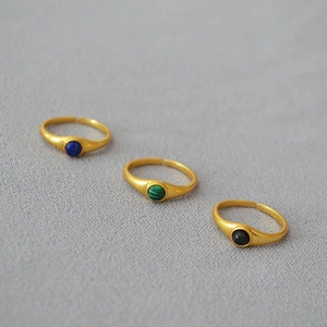 Three adjustable gold rings with inset blue, green and black stones on grey fabric